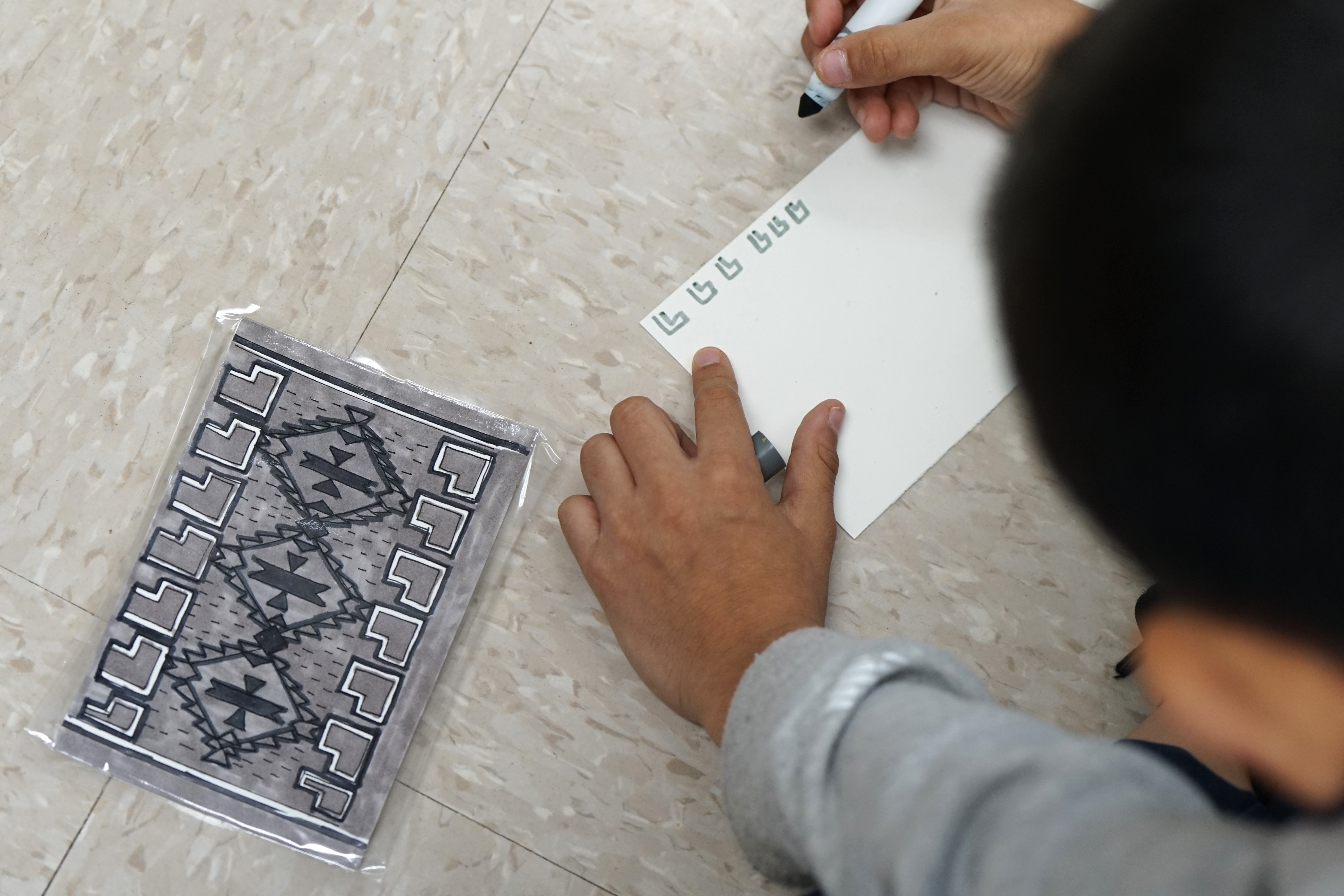 A boy starts drawing his rug design with a grey marker