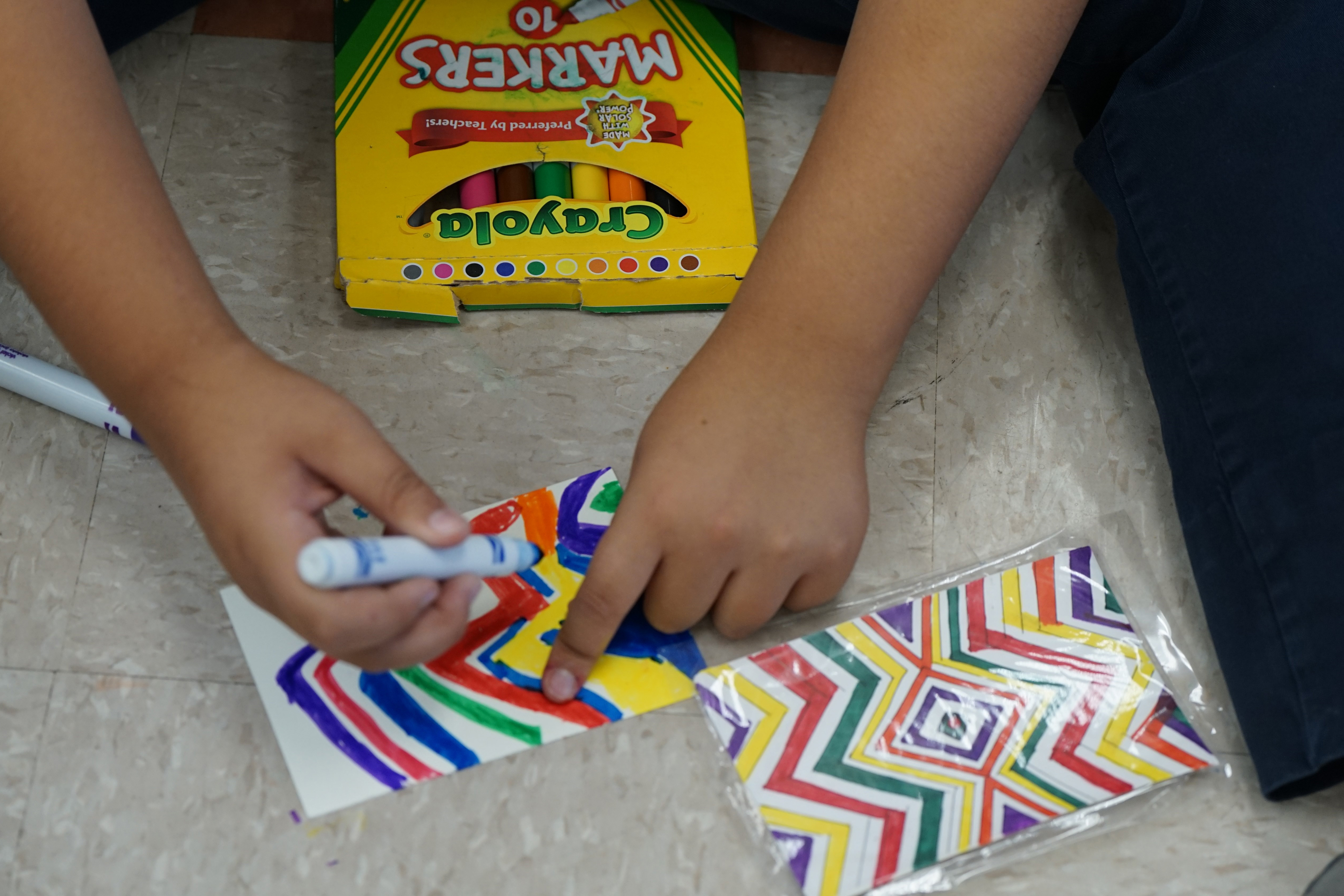 A student draws their colorful rug design with a blue marker