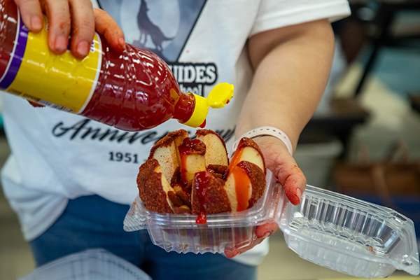A woman pours hot sauce on apple slices