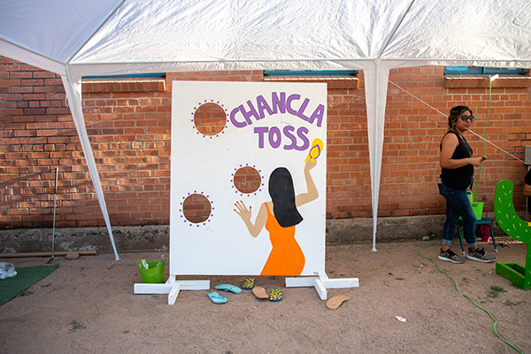 A woman stands next to a carnival game board for the Chancla Toss