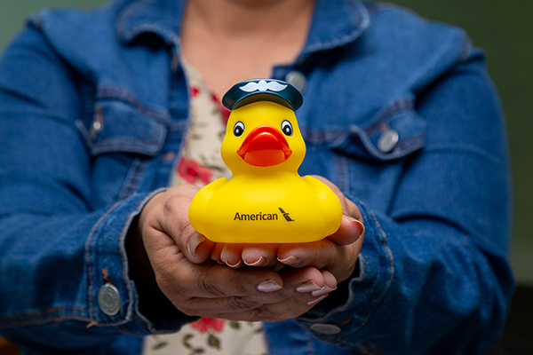 A woman holds out a rubber duck from American Airlines wearing a pilots hat